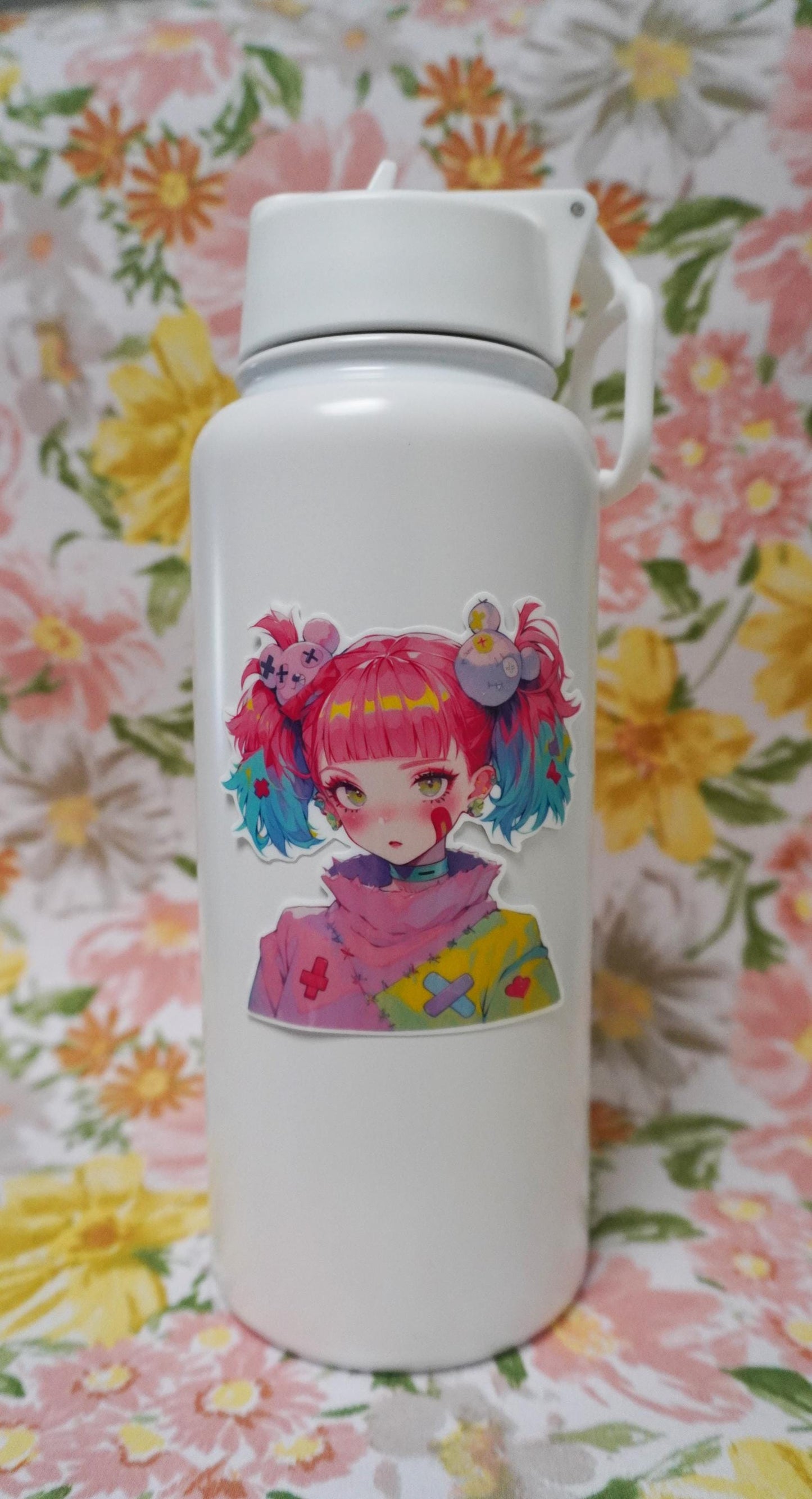 A white water bottle with a colorful anime-style sticker of a girl with pink and blue hair in pigtails, set against a floral-patterned background in soft pastel colors.