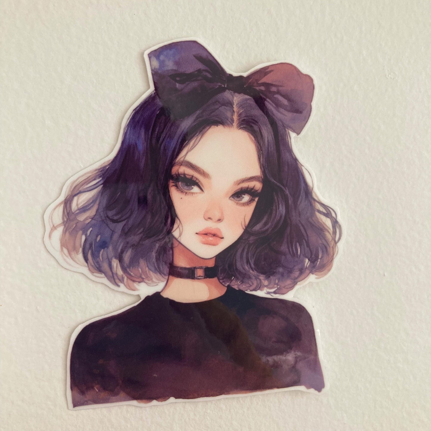 A sticker of an anime-style character with short dark purple hair, a large bow, and a black choker, placed on a plain white surface.