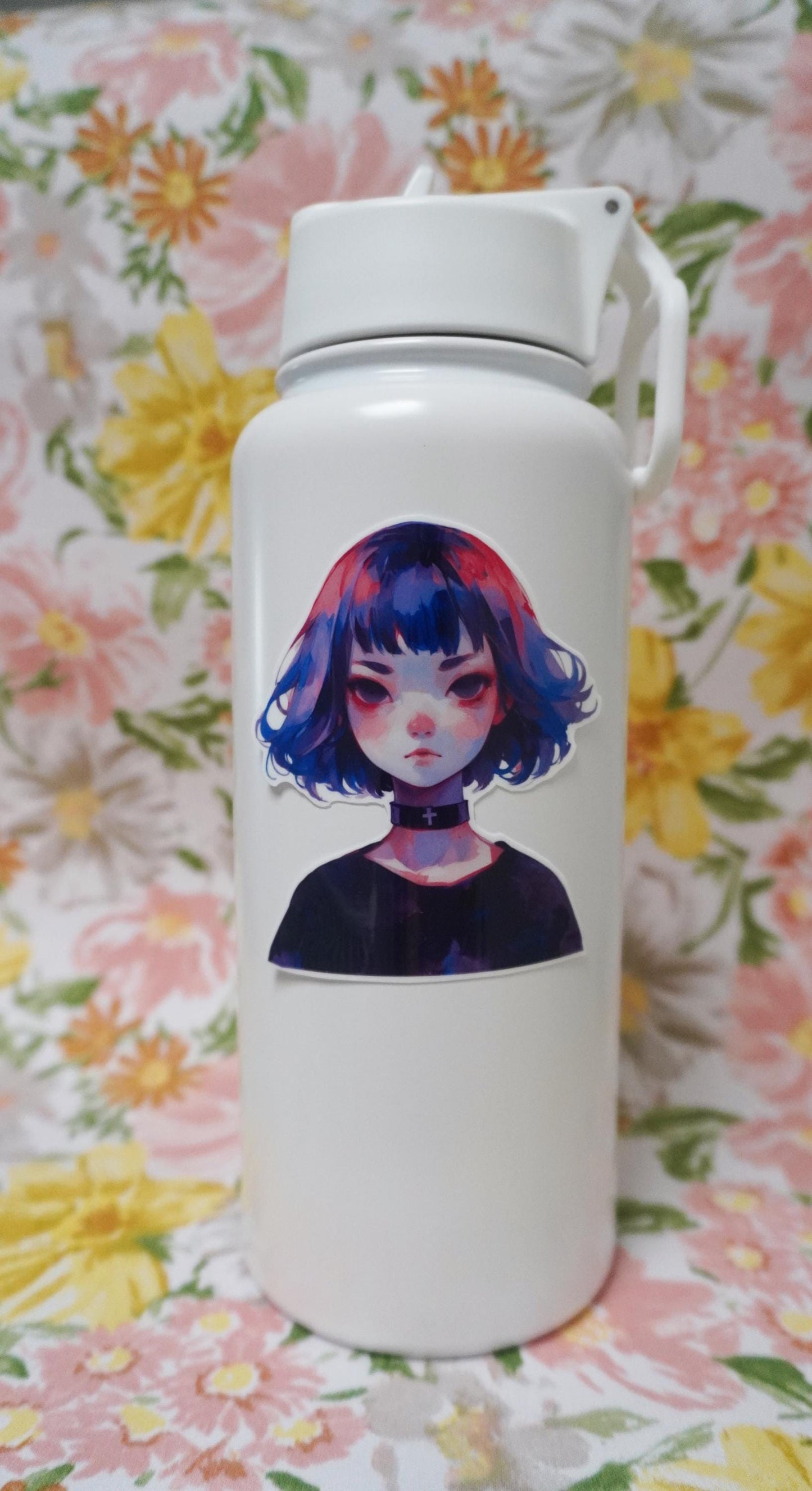 A white bottle with a sticker of an anime-style character with a short bob haircut in blue and pink, wearing a black choker with a white cross. The bottle is set against a floral background with pink, yellow, and green tones.