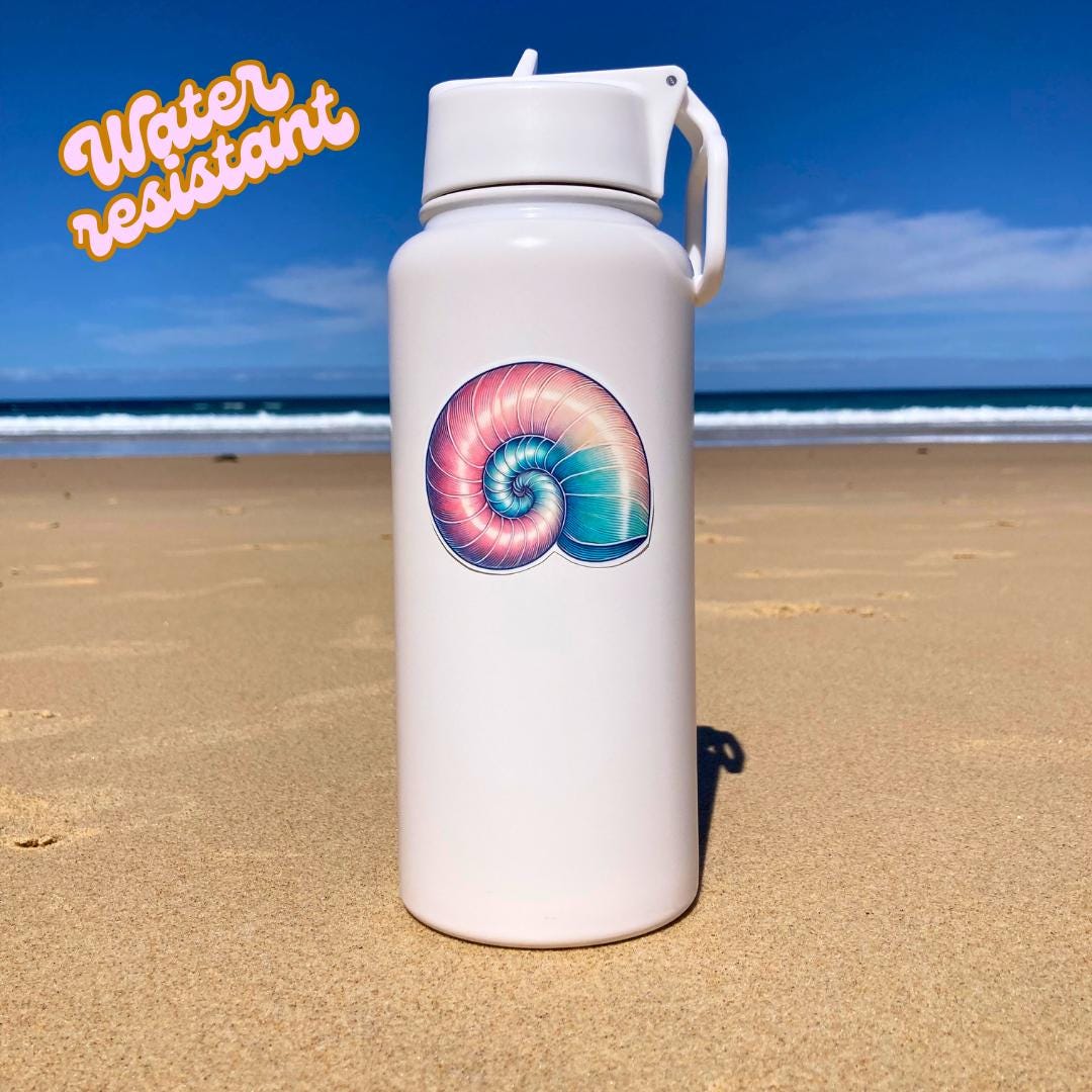 A white water bottle with a colorful nautilus shell sticker in pink, blue, and purple hues is placed on a sandy beach. The background shows the ocean and a clear sky. The words "Water resistant" are in the top left corner, highlighting durability