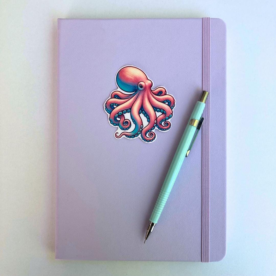 A pastel purple notebook with an elastic band features a colorful octopus sticker in pink and blue hues. A light blue mechanical pencil with gold accents rests diagonally on top. The simple background highlights the notebook and stationery items.