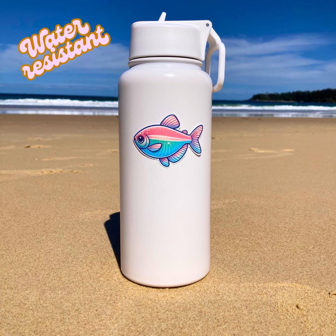 A white bottle sits on a sandy beach, decorated with a colorful tetra fish sticker in shades of pink, teal, and blue. The background shows the ocean and a bright blue sky. "Water resistant" text is seen in orange in the upper left corner.