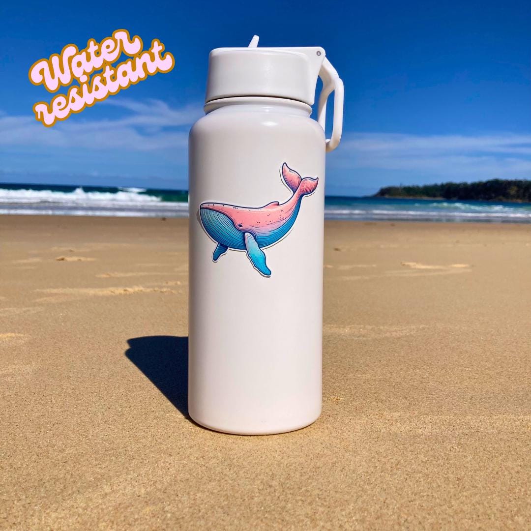 A white water bottle with a colorful whale sticker in pink and blue hues is placed on a sandy beach. The background shows the ocean and a clear sky. The words "Water resistant" are in the top left corner, highlighting the sticker's durability
