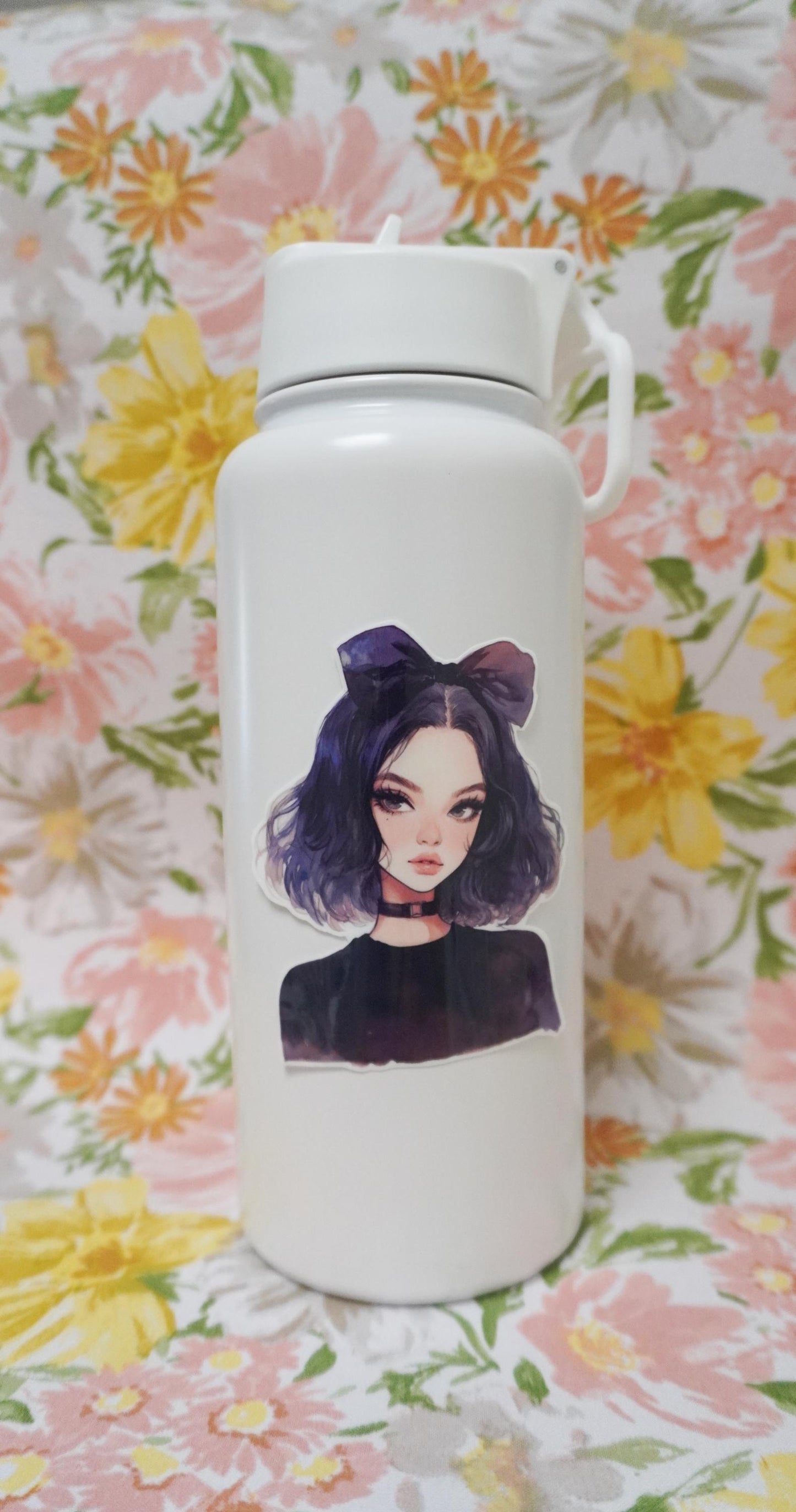 A white water bottle with a sticker of an anime-style character with dark purple hair, a large bow, and a black choker, set against a floral-patterned background.