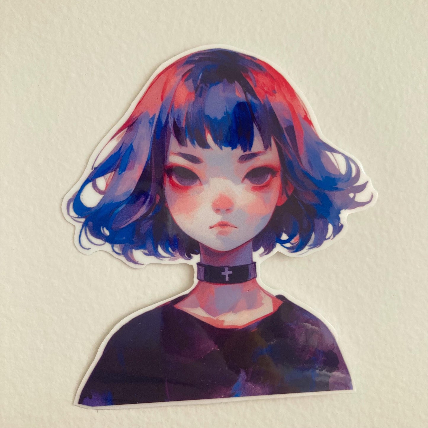 Sticker of an anime-style character with a short bob haircut, colored in shades of blue, pink, and purple. The character has a somber expression, dark eyes, and is wearing a black choker with a cross on it. Background is a plain light-colored surface