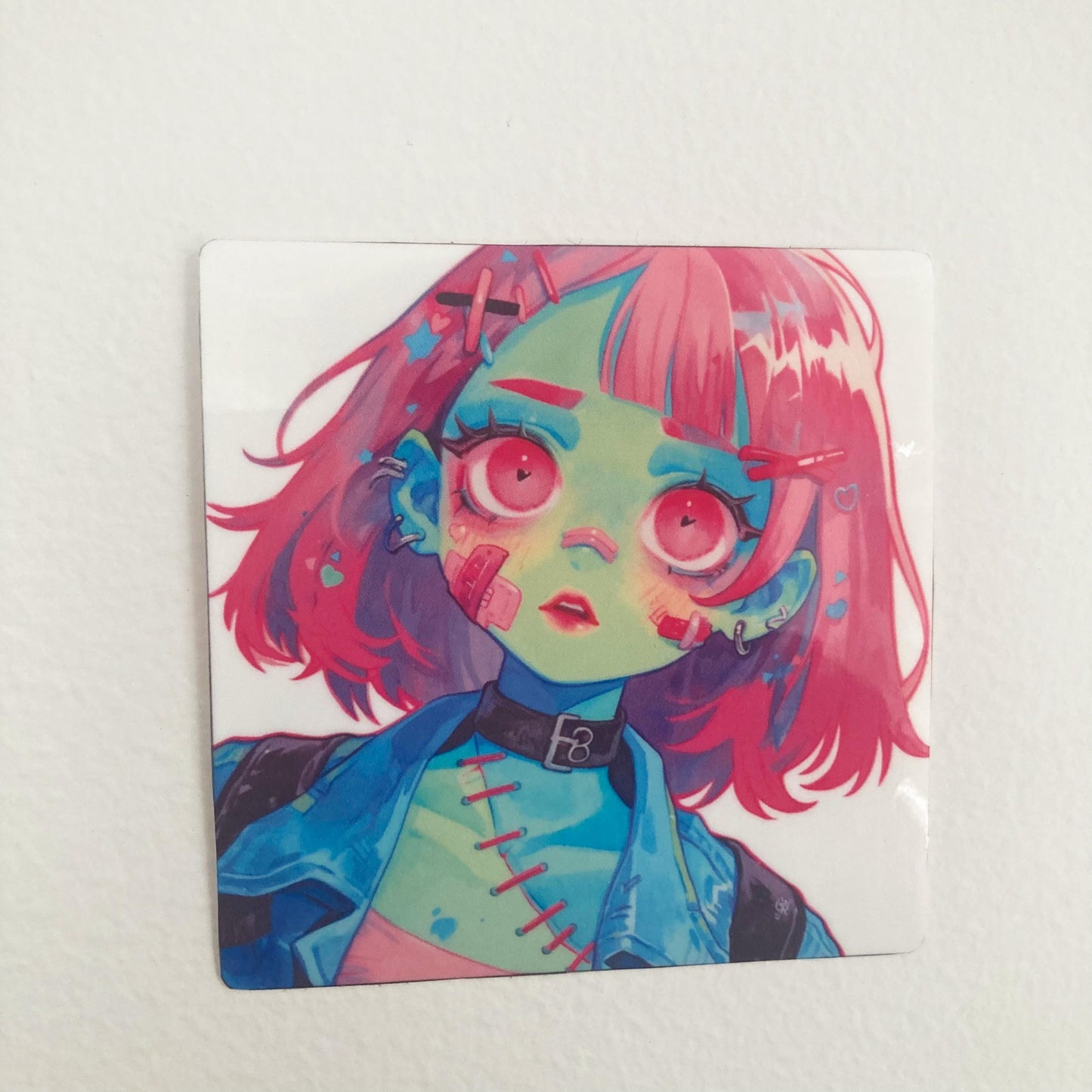 A sticker of a girl character with green skin, large pink eyes, pink hair, and stitched details on their face and chest. The character wears a blue jacket and a black choker, with a sad or dazed expression.