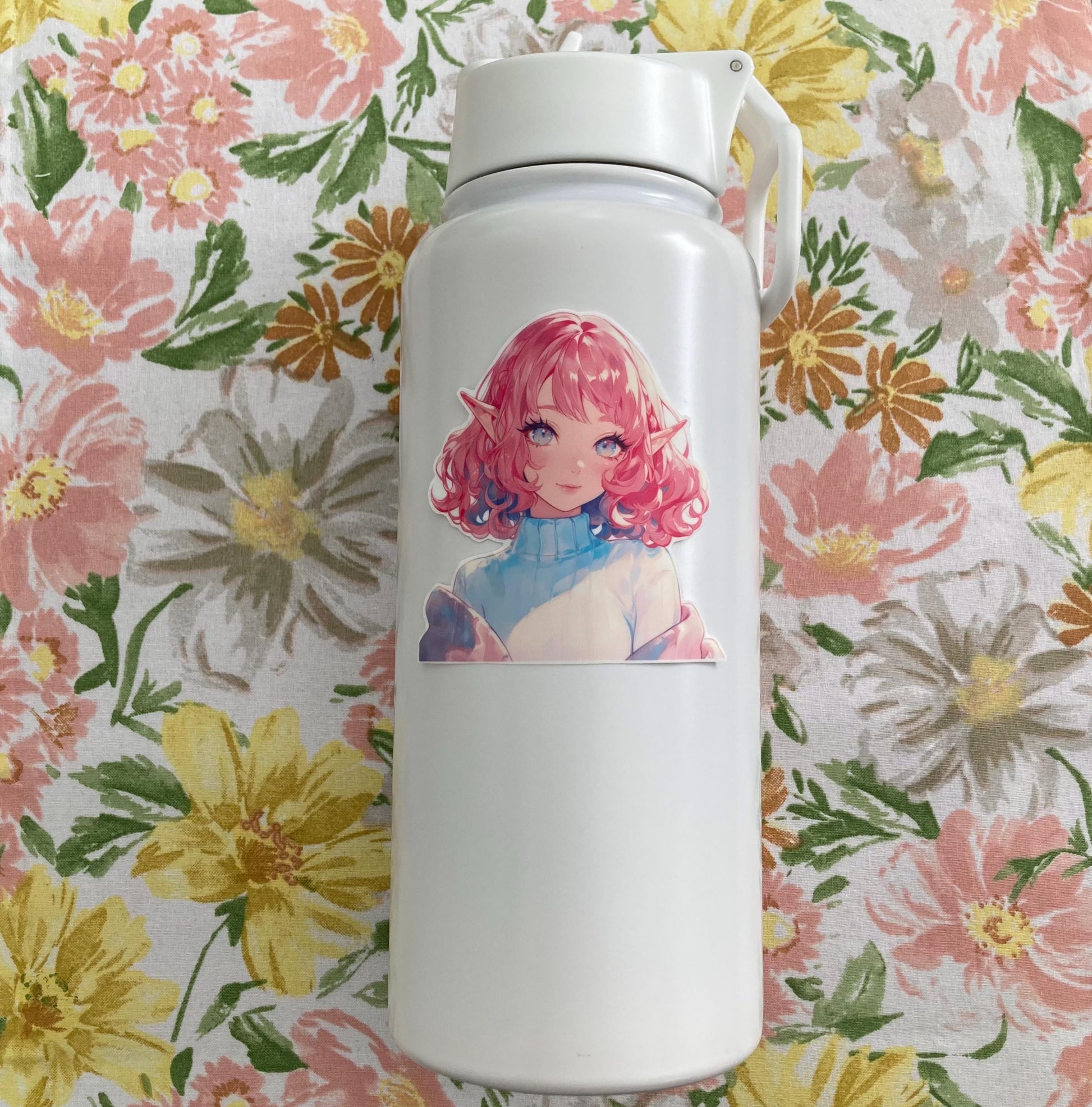 A white water bottle with an anime sticker featuring a character with curly pink hair, elf ears, and bright eyes in a turtleneck. The background is a floral fabric with pink, yellow, and green flowers, complementing the sticker&#39;s pastel colors.