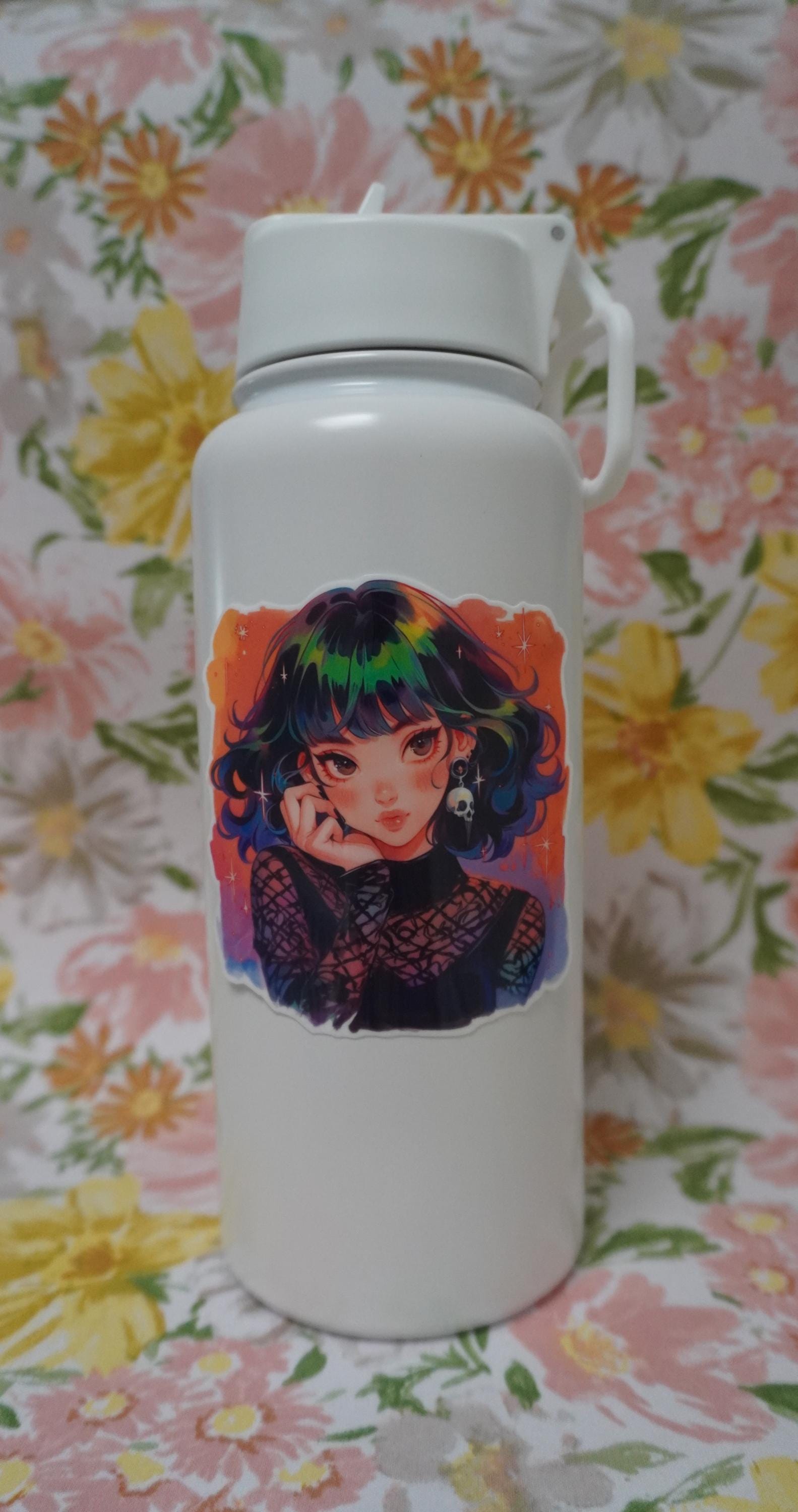 A white water bottle with a colorful anime sticker featuring a girl with rainbow hair, a skull earring, and a gothic mesh outfit. The sticker&#39;s vibrant design stands out against a floral background with pink, yellow, and green flowers.