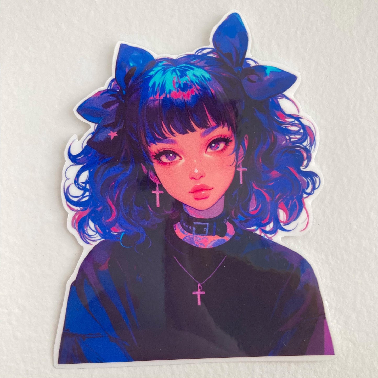 A sticker of an anime-style character with curly blue and pink hair, large bows, cross earrings, and a black choker, placed on a plain white surface.
