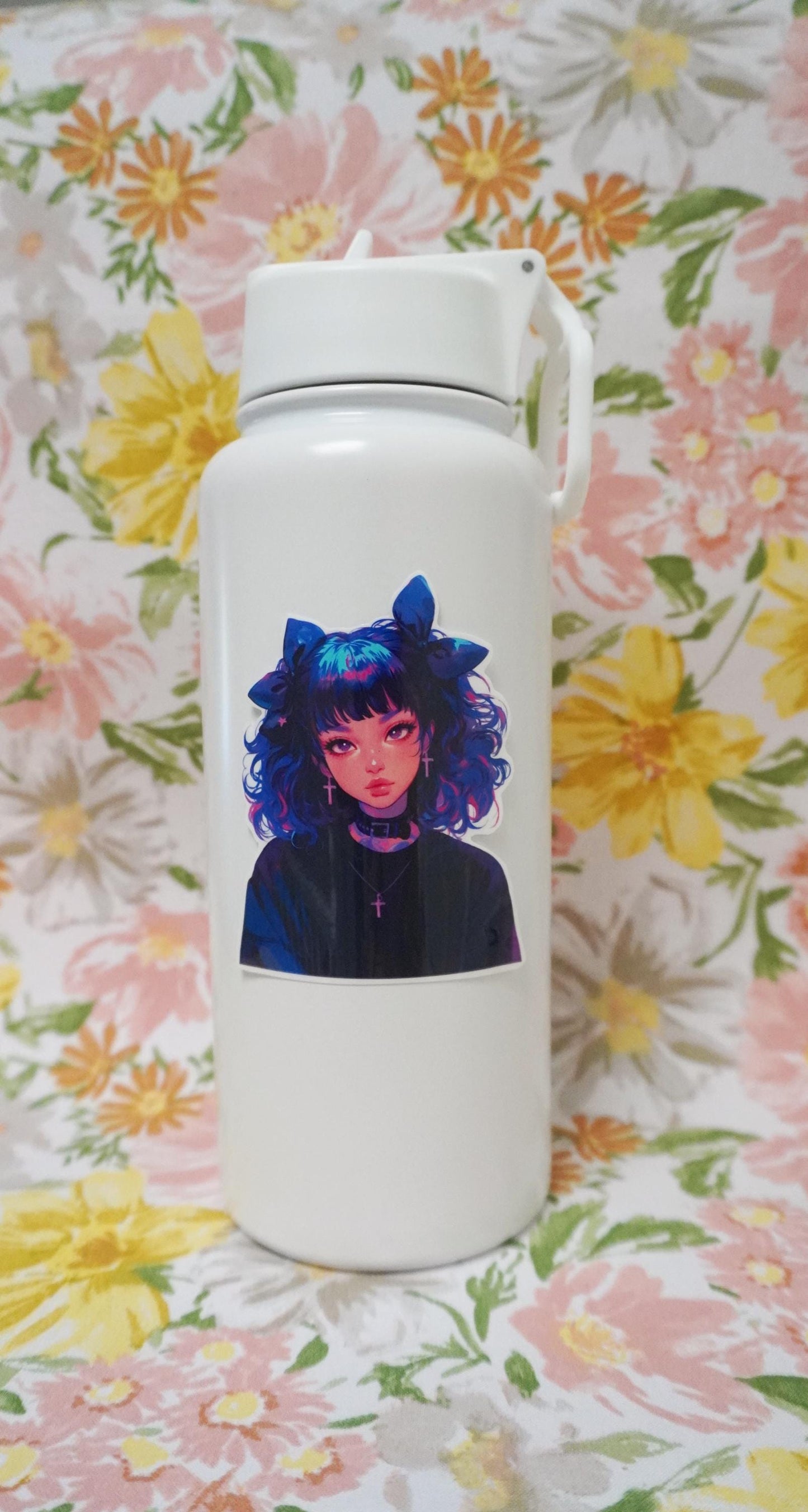 A white water bottle with a sticker of an anime-style character with curly blue and pink hair, large bows, cross earrings, and a black choker, set against a floral-patterned background.