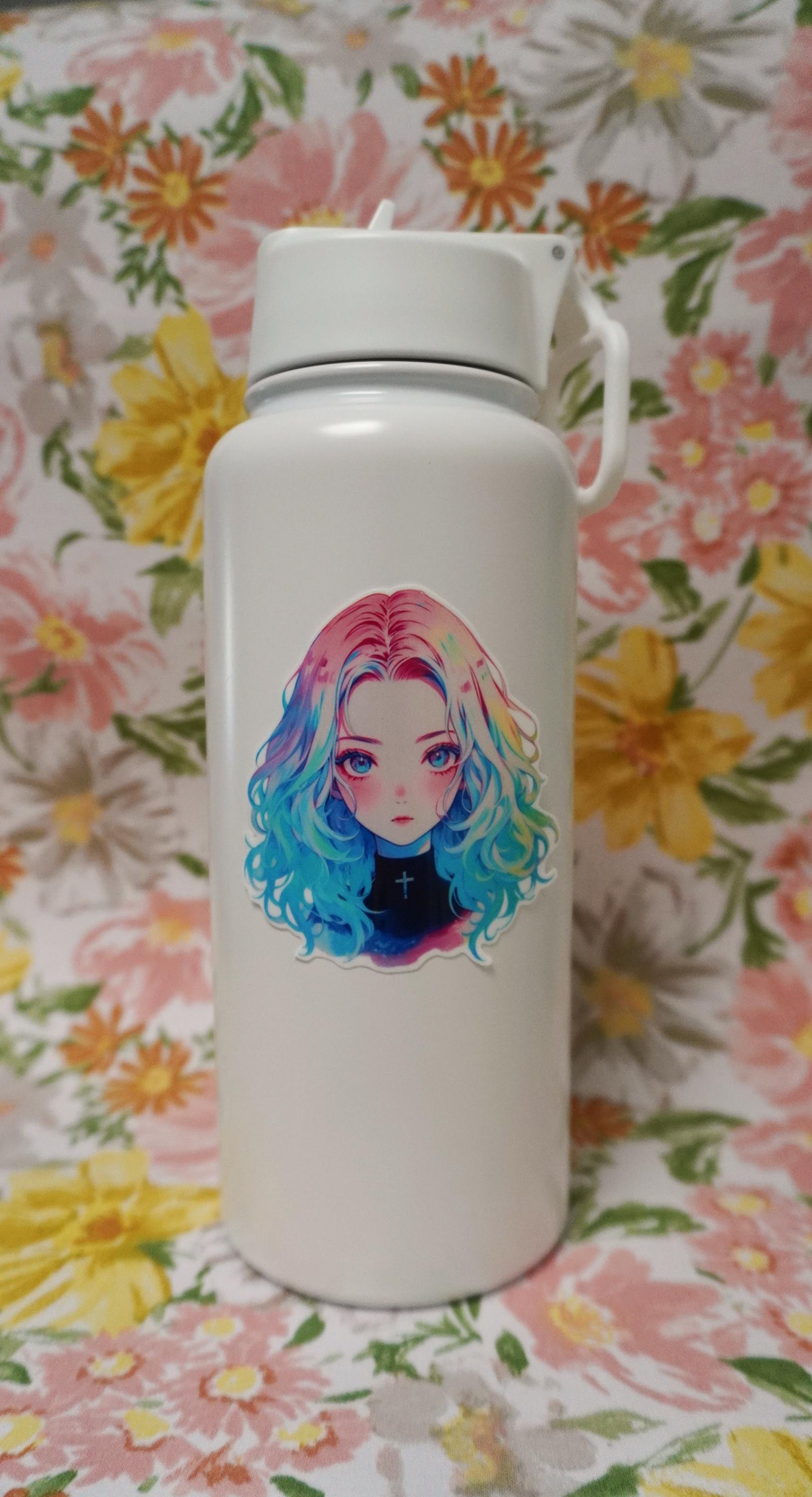 White bottle with a sticker of an anime girl with rainbow hair and a black top featuring a cross. The background is a floral fabric with large pink, yellow, and green flowers.