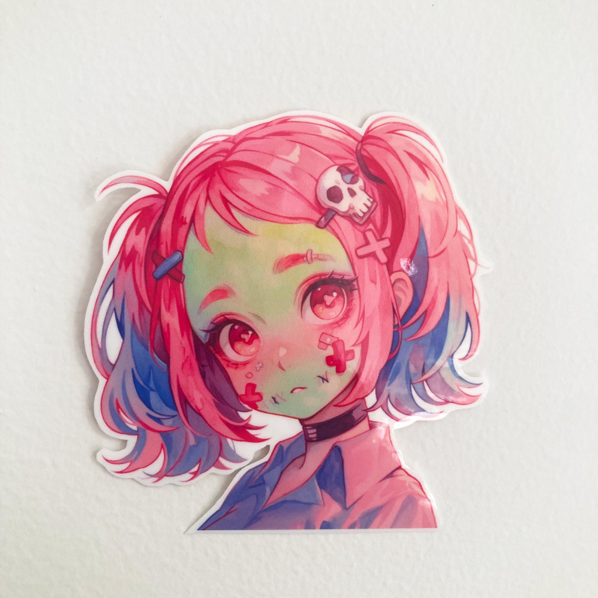 A sticker of an anime character with pink and blue hair, red eyes, and a skull hair accessory, placed on a light-colored background.