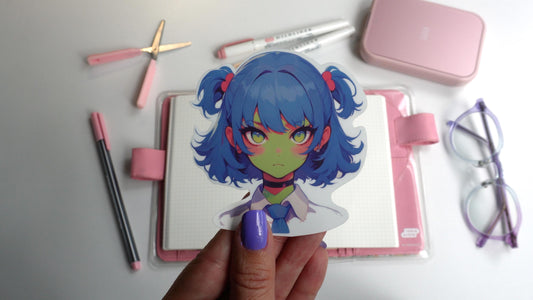 A sticker of an anime-style character with blue twin-tails, pink hair ties, green skin, and yellow eyes, wearing a white shirt, blue tie, and black choker. The sticker is held up by a hand with purple-painted nails.