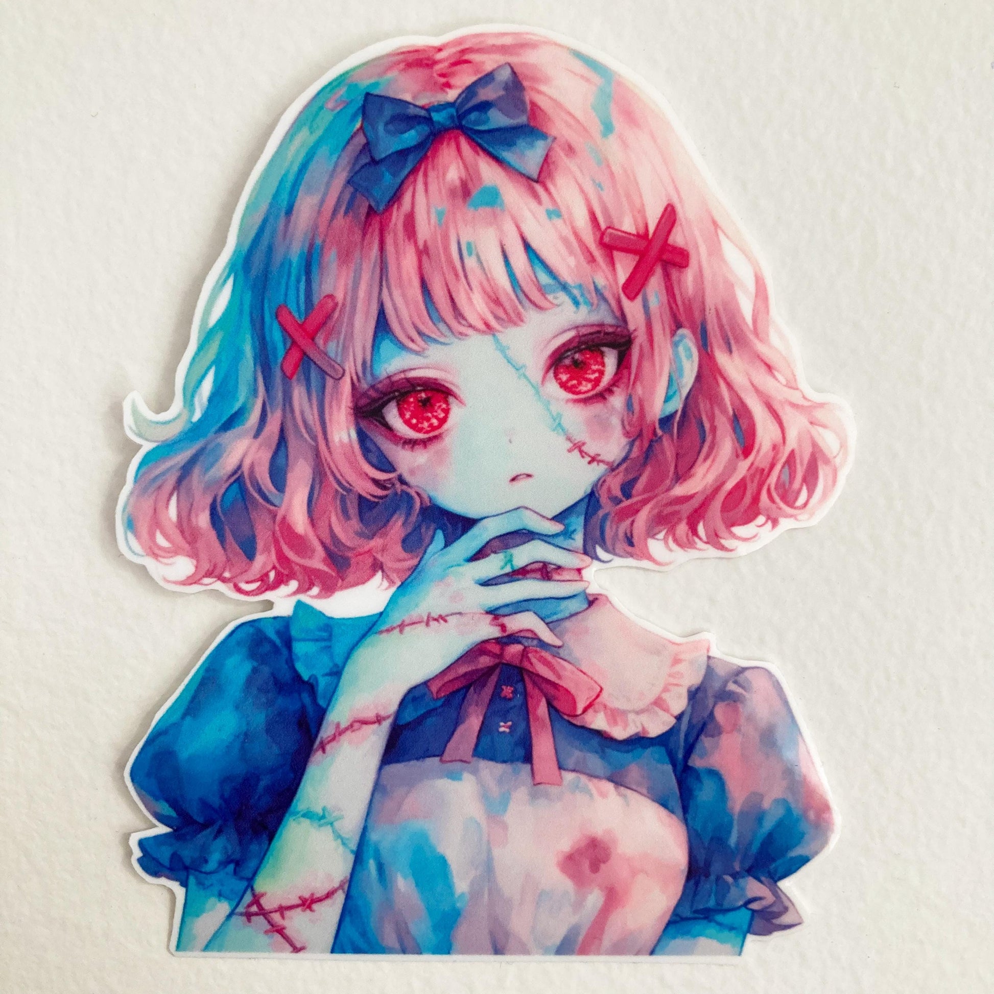 A colorful anime-style sticker of a girl with pink hair, red eyes, and stitches on her skin. She wears a blue dress with a white collar and a bow, gazing forward with her hand near her face. The sticker is placed on a white surface.