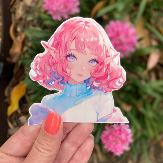 A hand with coral nail polish holding an anime sticker of a character with curly pink hair, elf ears, and bright eyes wearing a turtleneck. In the background are blurred pink flowers and greenery, adding a natural contrast to the sticker&#39;s colors.