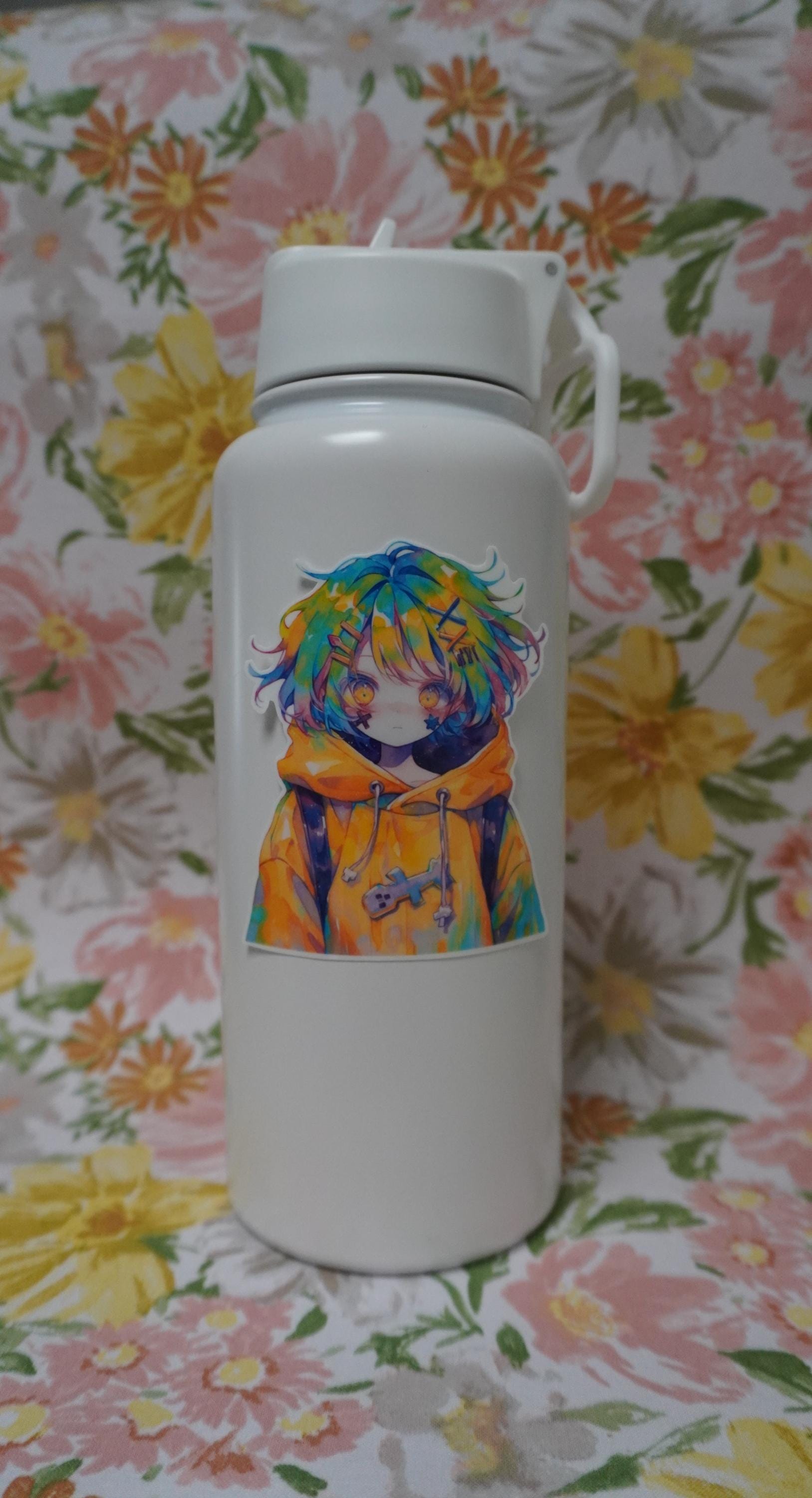 A white water bottle with a anime sticker featuring a character with multicolored hair and a yellow hoodie. The background is a floral pattern with pink, yellow, and green flowers, enhancing the bright, colorful aesthetic of the sticker and bottle