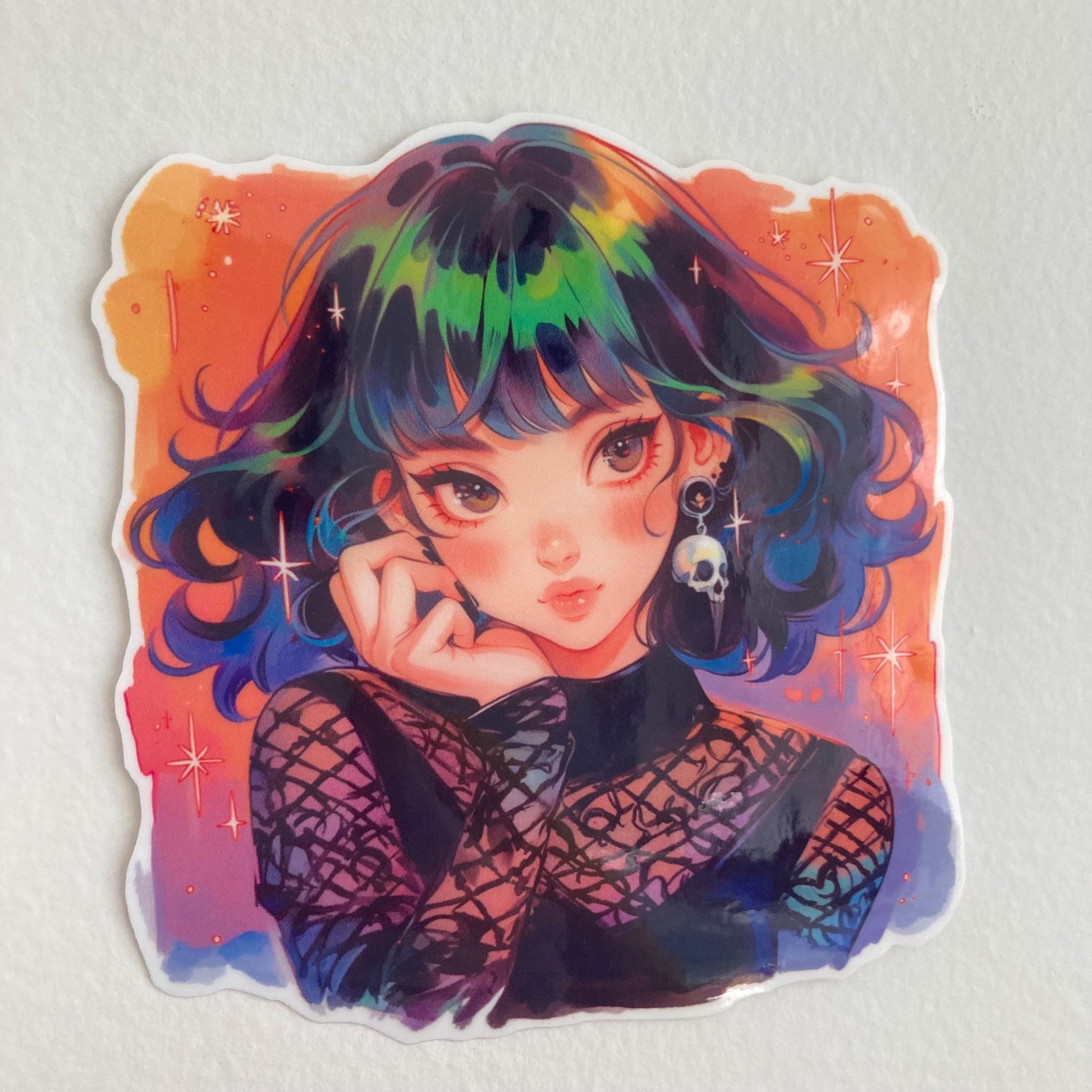 A colorful anime sticker of a girl with rainbow hair star accents, and a skull earring, set against a vibrant orange background with sparkles. She wears a gothic mesh outfit, and the sticker is on a plain, light-colored surface to showcase its detail