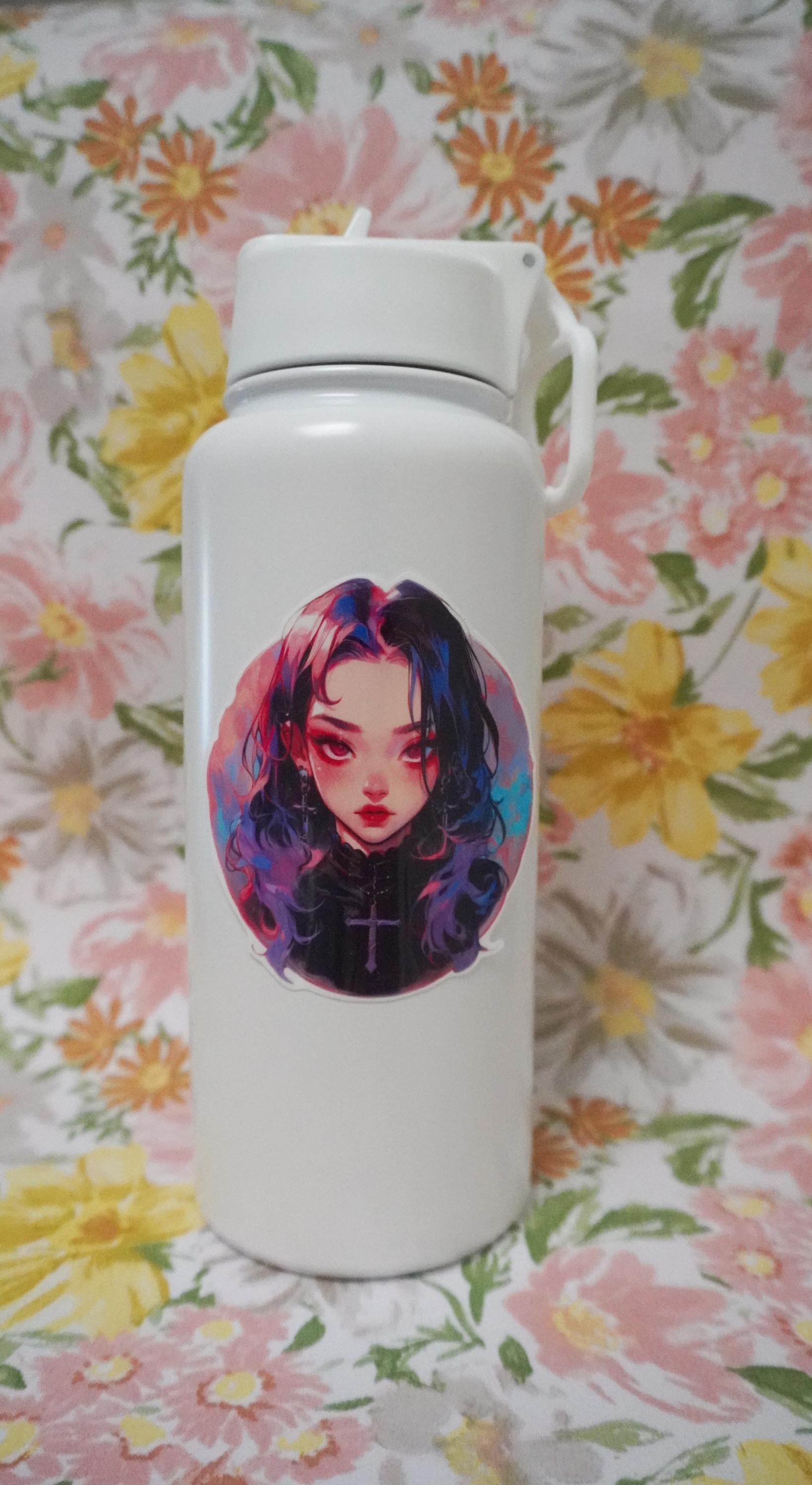 A white water bottle decorated with a colorful anime-style sticker of a girl with dark hair streaked in pink and blue, wearing a cross necklace. The background is a floral pattern with pink, yellow, and green colors, enhancing the aesthetic.