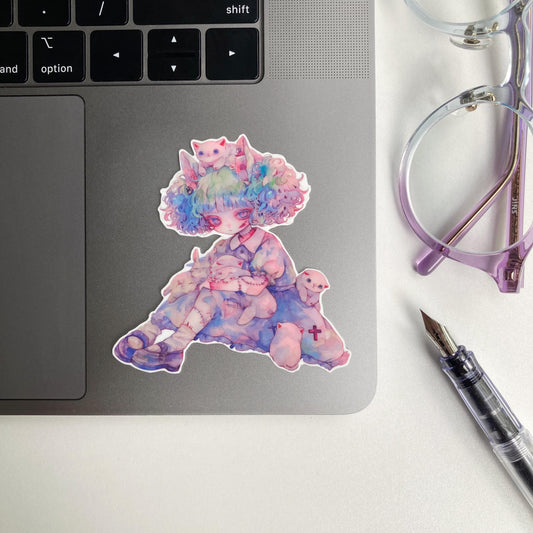 Sticker of an anime character with pastel curly hair sitting with white cats and bunnies, wearing a blue dress and stitched limbs. The sticker is placed on a laptop keyboard corner