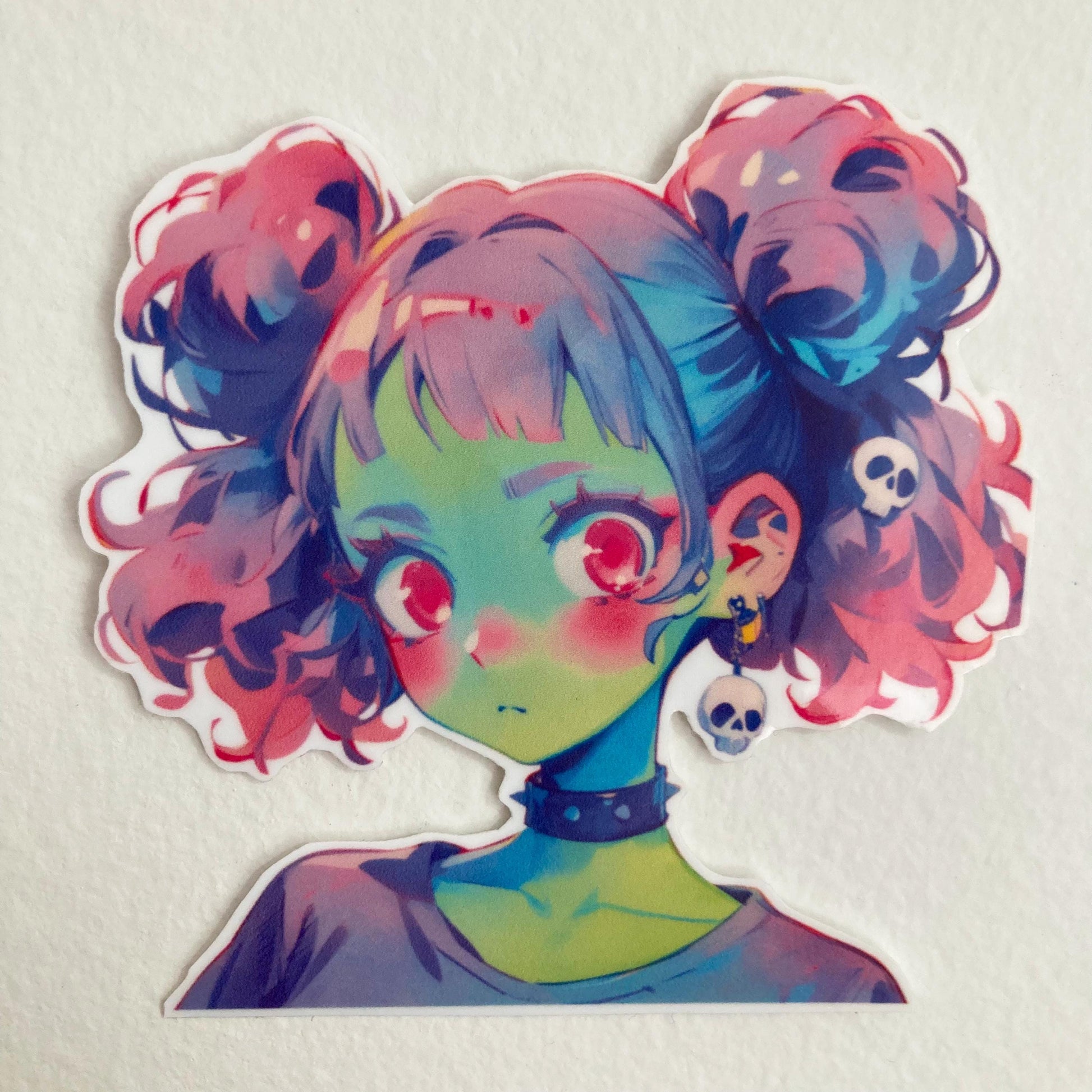 Sticker of an anime-style character with pastel pink and blue twin buns, green skin, and large pink eyes. The character wears a black choker and skull earrings, set against a plain background.